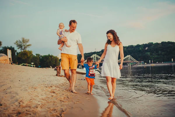 Concept vacances à la plage familiale. Famille de quatre personnes maman, papa et frères enfants garçons marchant, veulent pieds nus sur la rive de la rivière par la main au coucher du soleil en été — Photo