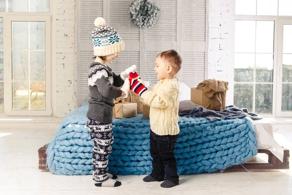 Niños hermano y hermana de pie y jugando en casa en el dormitorio cerca de la cama con cajas, regalos en el fondo de la decoración de Navidad un día soleado. — Foto de Stock