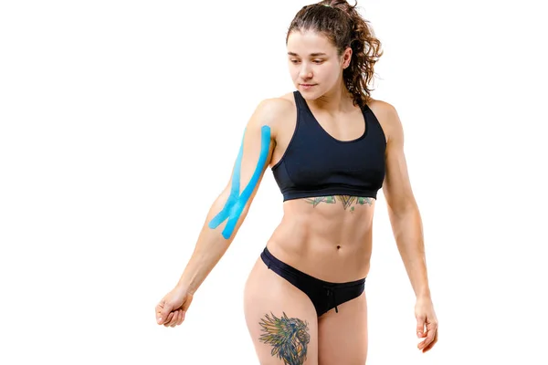 Concepto de medicina deportiva y salud. Una joven codeseada con una buena figura posando sobre un fondo blanco aislado con una cinta de kinesiología, una cinta azul pegajosa en su brazo. Medicina alternativa — Foto de Stock