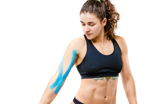 Concepto de medicina deportiva y salud. Una joven codeseada con una buena figura posando sobre un fondo blanco aislado con una cinta de kinesiología, una cinta azul pegajosa en su brazo. Medicina alternativa — Foto de Stock