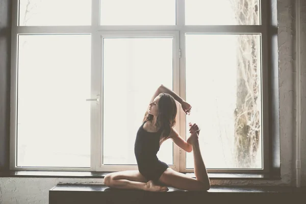 Bela dançarina menina com cabelos longos fluindo em roupas pretas, maiô, em uma bela pose bonita na grande janela Luz do dia, silhueta de um corpo bonito.Tema da dança Contemporânea e Clássica — Fotografia de Stock