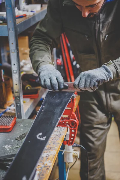 Чоловік-працівник у майстерні лижного сервісу ремонтує ковзну поверхню лиж. Крупним планом рука з пластиковим металобрухтом для видалення воску, видалення нового воску. Ремонт гірськолижного бордюру — стокове фото