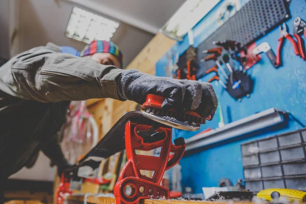 A man in work clothes, repairman in workshop ski service repairing the sliding surface of skis, Brushing, wax removal, final ski polishing. In the hands of an electric brush. Theme repair of ski curb