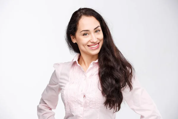 Porträt einer jungen Frau mit einem charmanten zahmen Lächeln, schwarzen Haaren und braunen Augen auf weißem Hintergrund in rosa Hemd. positive und freudige Emotionen — Stockfoto