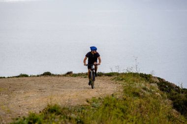Tema turizm ve dağ bisikleti bisiklet. adam Akdeniz'de İspanya kosta brava kask ve spor giyim kıyısında arka planı rocky, kayalık yol yokuş yukarı sürmek
