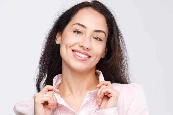 Retrato de cerca de una joven mujer muy hermosa con una encantadora sonrisa dentada, cabello negro y ojos marrones sobre un fondo blanco en una camisa rosa. Las manos cerca de la cabeza. Emociones positivas y alegres — Foto de Stock