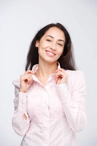 Portret van een jonge mooie Kaukasische vrouw met lange zwarte haren in een roze shirt is hand in hand op een kraag op een lichte achtergrond in de studio — Stockfoto