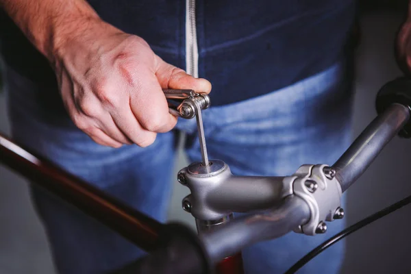 Thema Reparaturfahrräder. Nahaufnahme der Hand eines kaukasischen Mannes mit einem Sechskantschlüssel, um Vorbauten an einem Fahrrad zu installieren — Stockfoto