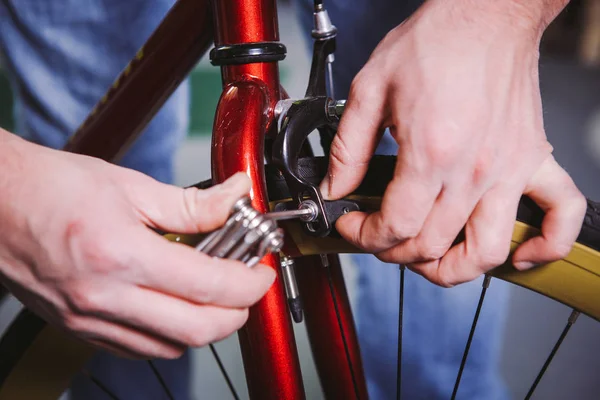 Thema Reparaturfahrräder. Nahaufnahme der Hand eines kaukasischen Mannes mit einem Sechskant-Handwerkzeug zum Einstellen und Anbringen von Felgenbremsen an einem roten Fahrrad — Stockfoto