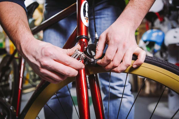 Thema Reparaturfahrräder. Nahaufnahme der Hand eines kaukasischen Mannes mit einem Sechskant-Handwerkzeug zum Einstellen und Anbringen von Felgenbremsen an einem roten Fahrrad — Stockfoto