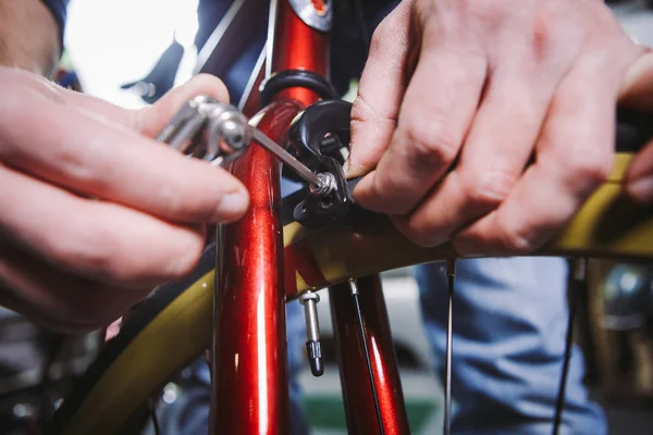 Thema Reparaturfahrräder. Nahaufnahme der Hand eines kaukasischen Mannes mit einem Sechskant-Handwerkzeug zum Einstellen und Anbringen von Felgenbremsen an einem roten Fahrrad — Stockfoto