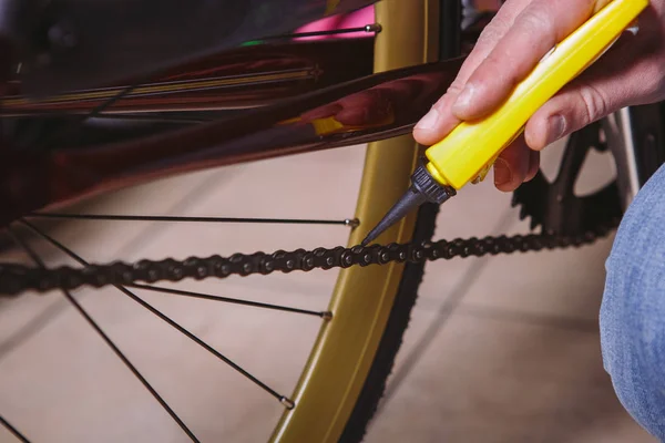 Theme repair bikes. Close-up of a Caucasian man\'s hand use a Chain Lubricant in a yellow lubricator for llubricator a bicycle chain on a red bicycle