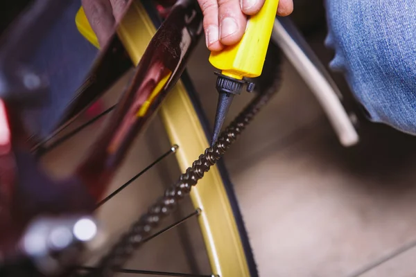Sepeda perbaikan tema. Close-up of a Caucasian man 's hand use a Chain Lubricant in a yellow lubricator for llubricator a bicycle chain on a red bicycle — Stok Foto