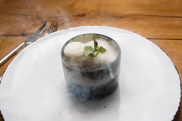 Postre dulce helado en un plato blanco sobre una mesa de madera en un retor italiano. Ingredientes helado blanco con menta y cacao en un vaso tequal transparente con humo . — Foto de Stock