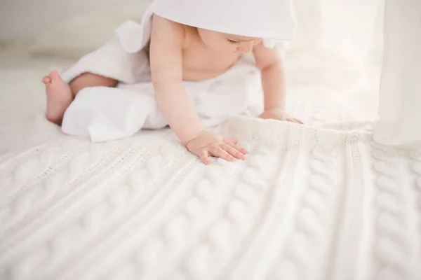 Красивый улыбающийся новорожденный мальчик, покрытый белым бамбуковым полотенцем с веселыми ушами. Сидя на белом трикотаже, шерстяной клетчатый яркий интерьер. Выход из окна — стоковое фото