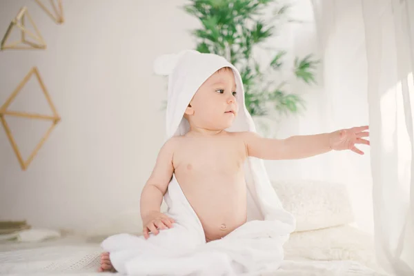 Mooie lachende pasgeboren babyjongen bedekt met witte bamboe handdoek met leuke oren. Zittend op een witte gebreide, wollen plaid helder interieur. De vlucht vanuit het venster — Stockfoto