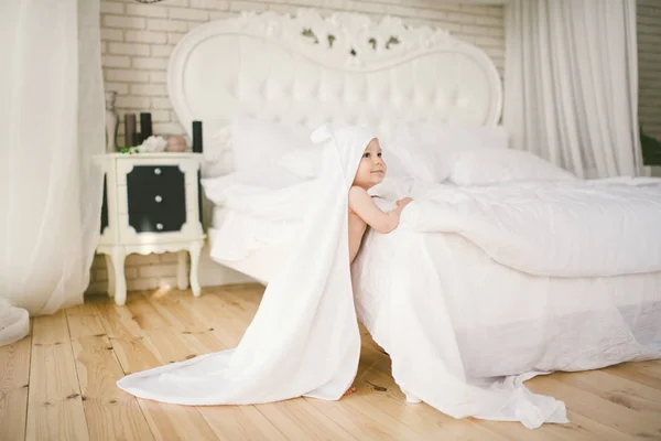 Bebê recém-nascido bebê de cinco meses de idade no quarto ao lado de uma grande cama branca no chão de madeira envolto em uma toalha de bambu branco . — Fotografia de Stock
