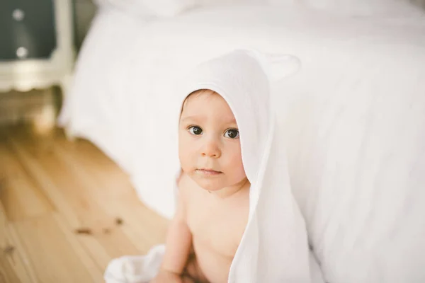 De vijf maanden oude baby pasgeboren baby in de slaapkamer naast een grote witte bed op de houten vloer gewikkeld in een handdoek met witte bamboe. — Stockfoto