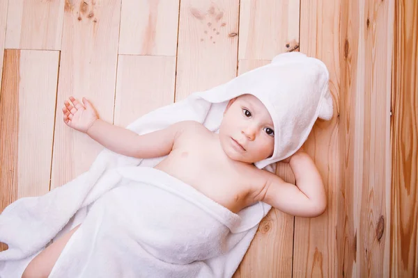 Jongetje met bruine ogen is vijf maanden oud verpakt in een witte handdoek met oren op houten achtergrond . — Stockfoto