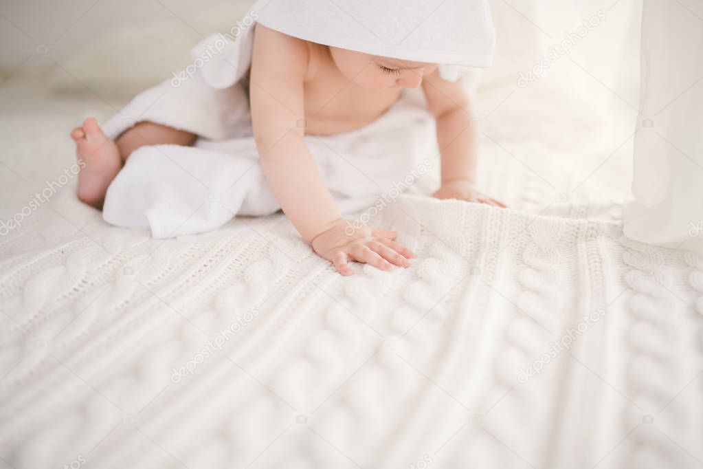 beautiful smiling newborn baby boy covered with white bamboo towel with fun ears. Sitting on a white knit, wool plaid bright interior. The ight from the window