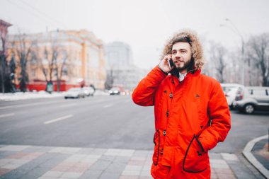 Sakal ve kırmızı ceket başlıklı bir öğrenci genç adam cep telefonu kullanır, üniversite veya kolej bina kırmızı zemin üzerine gülümseme ile telefonda konuşurken yakınındaki baş, elinde tutan