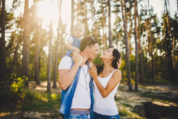 Famille maman, papa et fille s'assoit au papa sur les épaules, et les parents embrassent la nature dans la forêt en été au coucher du soleil — Photo