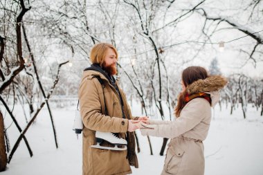 Kış ve tarih. Genç çift, aşık erkek ve kadın kış kar ve orman elele ve gülümseyen bir arka plan üzerinde. Uzun saçlı ve sakallı bir adam paten tutarak ve kıza baktığını