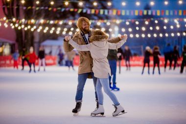 Tema buz buz pateni pisti ve sevgi dolu çift. genç, şık insanlarla tanışmak el ile şehir buz pateni pisti ampulleri ve ışıkları yaktı kalabalıkta binmek. Buz pateni Ice arena üzerinde Noel için kışın