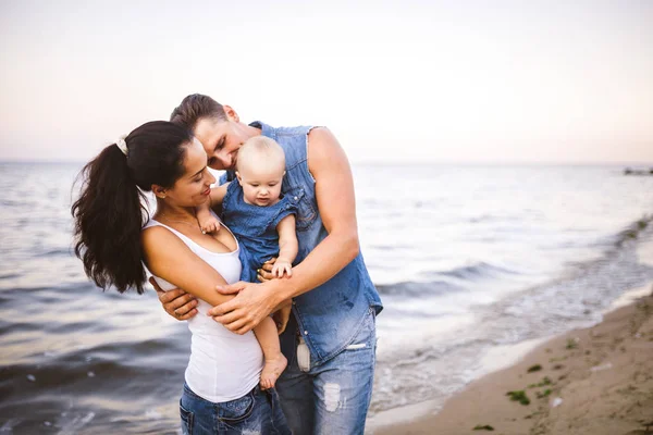 Güzel genç aile bebek ile tatilde. Babası sarışın kız onun kollarında tutar ve esmerler anne kocası sarılarak. Aile plaj tatil yaz denize yakın kavramı — Stok fotoğraf