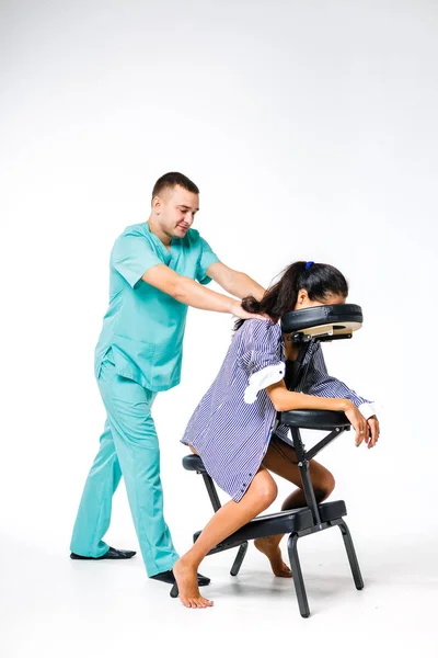 Tema masaje y oficina. Terapeuta masculino con traje azul haciendo masaje de espalda y cuello para trabajadora joven, mujer de negocios con camisa en silla de masaje shiatsu — Foto de Stock