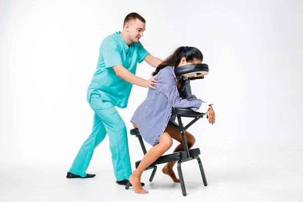 Tema masaje y oficina. Terapeuta masculino con traje azul haciendo masaje de espalda y cuello para trabajadora joven, mujer de negocios con camisa en silla de masaje shiatsu — Foto de Stock