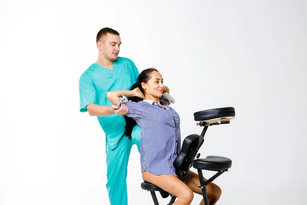 Tema masaje y oficina. joven terapeuta masculino en traje azul haciendo masaje de espalda con la rodilla apoyada en la columna vertebral de la trabajadora, mujer de negocios con camisa en la silla de masaje shiatsu para aliviar la fatiga — Foto de Stock