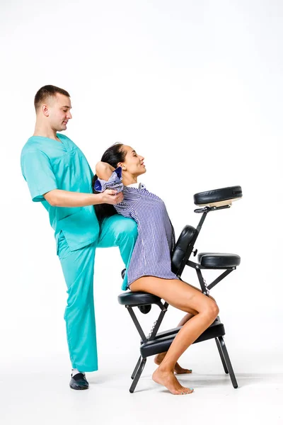 Tema masaje y oficina. joven terapeuta masculino en traje azul haciendo masaje de espalda con la rodilla apoyada en la columna vertebral de la trabajadora, mujer de negocios con camisa en la silla de masaje shiatsu para aliviar la fatiga — Foto de Stock