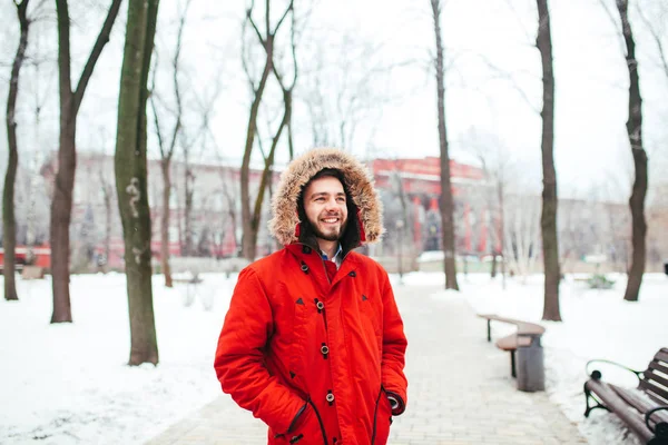肖像画、フードやファーは彼の頭の上に赤いジャケットを着たひげ笑みを浮かべて若いおしゃれな服を着て男のクローズ アップ。冬と霜テーマ — ストック写真