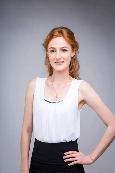 Retrato vertical hasta la cintura joven, hermosa mujer de negocios, estudiante con el pelo lred, rizado y pecas sobre fondo gris. SHe vestido con una blusa blanca con mangas cortas sobre hombros abiertos — Foto de Stock