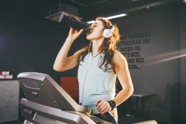 Spor ve beslenme ve egzersiz. Güzel bir genç kadın bir şişe, bir spor izle, güneşli havalarda elinde bir koşu bandı üzerinde çalışan spor salonunda siyah bir shaker protein içecekler