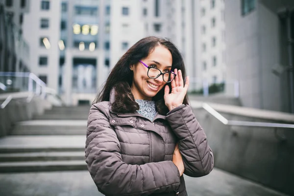 Portre güzel genç iş kadını esmer ceket ve kazak arka ofis görmek için gözlük İş Merkezi Binası, üzerinde duruyor. El gözlük kelepçeyi tutan ve uzağa arıyorsunuz — Stok fotoğraf