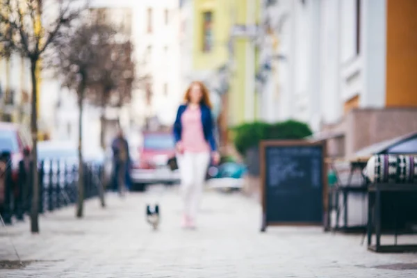 Розмитість фону A Рудий кавказьких брюнетки ходьба по європейських вулиці з Малі собаки породи Чихуахуа двох кольорів на повідку. Дівчина одягла на шкіряний піджак і рожевий взуття — стокове фото