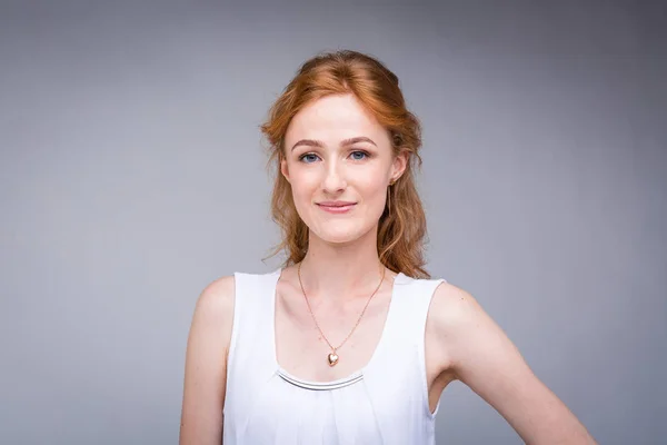 Primer plano retrato joven, hermosa mujer de negocios, estudiante con lred, pelo rizado y pecas en la cara sobre fondo gris en el estudio. Vestido con blusa blanca con mangas cortas sobre hombros abiertos — Foto de Stock