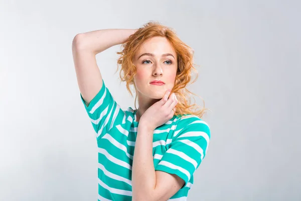 Retrato de cerca de una joven y hermosa mujer con el pelo rizado rojo en un vestido de verano con tiras de azul en el estudio sobre un fondo gris. Tema de vacaciones de verano, turismo y ropa de verano —  Fotos de Stock