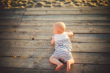 Yeni doğan çocuk A çocuk, bir yıl eski, gün günbatımında ahşap bir iskele, bir iskele Çizgili kıyafetler, üstten görünüm, bir yaz compline karnına yatıyor. Tema bir yaz aile tatil