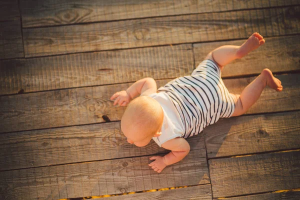 Νεογέννητο παιδί, ένα αγόρι, ένα χρονών, ξαπλωμένο με το στομάχι σε μια προβλήτα με τα ριγέ ρούχα, μια κάτοψη, μια ξύλινη αποβάθρα, ένα καλοκαίρι Απόδειπνο στο ηλιοβασίλεμα της ημέρας. Θέμα της οικογενειακές διακοπές καλοκαίρι — Φωτογραφία Αρχείου