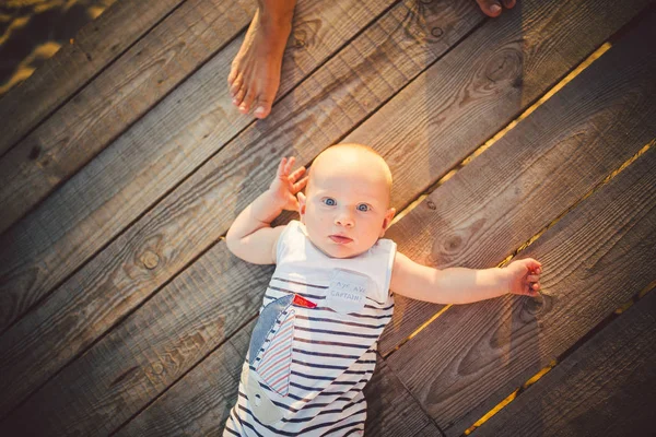 生まれたばかりの赤ちゃん男の子 1 年金髪の夏の日の夕暮れ時に彼の木製の背景埠頭に戻る、上、compineison からストライプ服ビューで桟橋の上に横たわる。夏の家族旅行のテーマ — ストック写真
