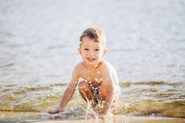 Junge Kind spielt macht Spritzer, schlägt Hände auf dem Wasser im Fluss bei Sonnenuntergang des Tages — Stockfoto