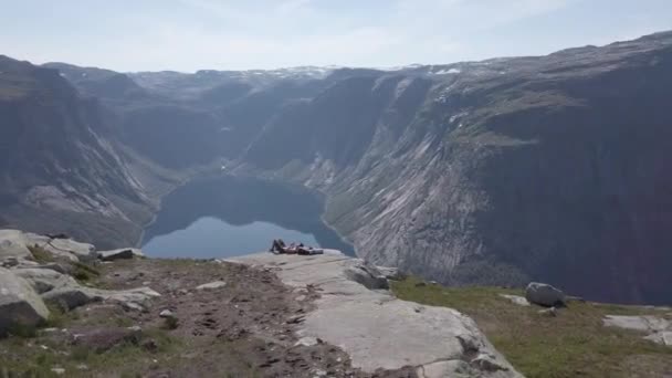 26 de julho de 2019. Noruega. homem sonhador deitado em pedra, relaxando depois de caminhar no topo da montanha penhasco com fiorde de água azul no fundo. Noruega viagem, conceito de liberdade. turista na montanha superior usa telefone — Vídeo de Stock