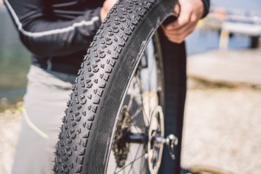 Bisiklet Tamiri. Dağ Motorunu Tamir Eden Adam. Bisikletli adamın arka tekerlek kazasında başı dertte. Adam İtalya 'da göl kenarındaki arka plandaki dağlarda bisiklet tamir ediyor. Bisikletçi dışarıda bisiklet tekerleğini tamir ediyor.