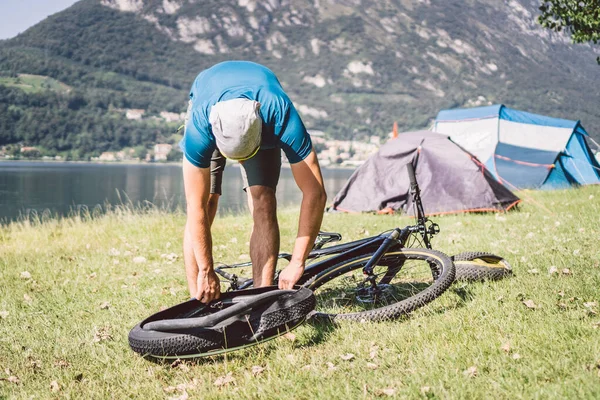 自転車修理。マウンテンバイクを修理する男。事故のトラブル後輪ケースにサイクリストの男。男はイタリアの背景の山の湖の近くの自転車を修正します。自転車を屋外で修理するサイクリスト — ストック写真