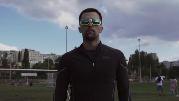 Le 2 mars 2019. Thème sport et santé. Portrait d'un jeune homme caucasien en tenue de sport et lunettes de soleil. Cours de sport d'entraînement au tapis roulant de piste de stade de la ville. Runner jogging en plein air — Video