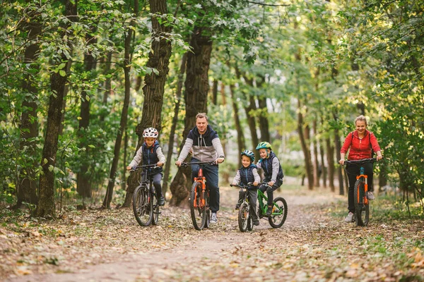 Rodziców i dzieci jeżdżących po leśnym szlaku. Młoda rodzina w ciepłych ubraniach jeździ na rowerze w jesiennym parku. Rodzinny rower górski po lesie. Rodzina tematyczna aktywny sport rekreacja na świeżym powietrzu. — Zdjęcie stockowe