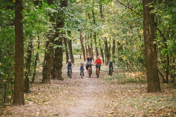 森の中をサイクリングしている親や子供たち秋の公園での若い家族のサイクリング。森で家族のマウンテンバイク。テーマ家族のアクティブなスポーツ屋外レクリエーション。秋の森を巡るファミリーサイクリング — ストック写真